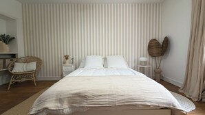 Een slaapkamer met een bed, nachtkastje, stoel en wand met verticale strepen.