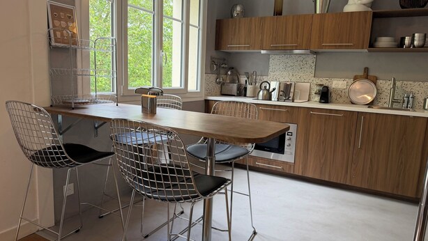 Een moderne keuken met een houten tafel, draadstoelen en roestvrijstalen apparatuur.