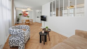 Un salon moderne avec un canapé, un coin repas comprenant une table et des chaises, un téléviseur fixé au mur et une grande fenêtre.