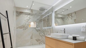 Une salle de bain moderne avec un mur en marbre, une cabine de douche en verre, un meuble-lavabo en bois et un grand miroir.