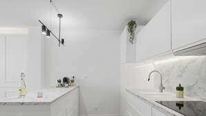 Une cuisine moderne avec des meubles blancs, un plan de travail en marbre, un four encastré et une plante suspendue.