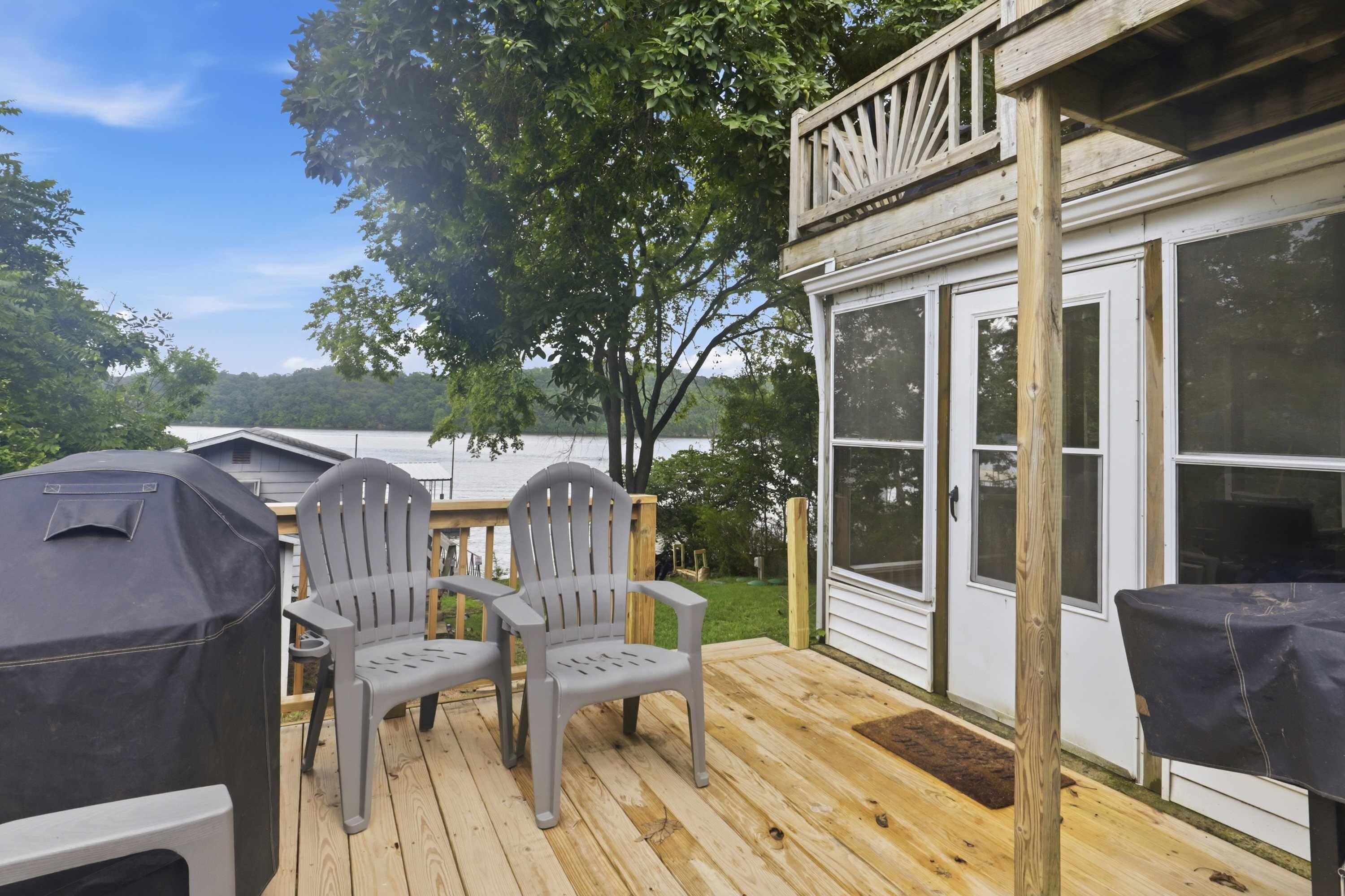 A deck with two Adirondack chairs, a grill, and a covered patio area.