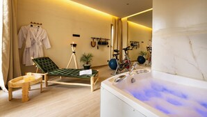 Ein Wellnessraum mit Massagesessel, einem kleinen Tisch mit Kerzen, einer Massageliege und einer Whirlwanne.