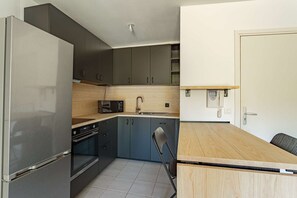 A compact kitchen with a refrigerator, oven, microwave, and a wooden dining table. - Charming one-bedroom apartment with a terrace and parking near Bayonne (BAYONNE)