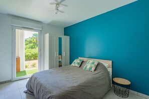 A bedroom with a bed, a ceiling fan, a round table, and a view through a sliding door to an outdoor area. - Charming one-bedroom apartment with a terrace and parking near Bayonne (BAYONNE)