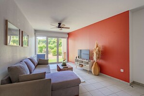 A living room with a sofa, TV, and a large window. - Charming one-bedroom apartment with a terrace and parking near Bayonne (BAYONNE)