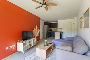 A living room with a TV, sofa, wooden coffee table, and a ceiling fan. - Charming one-bedroom apartment with a terrace and parking near Bayonne (BAYONNE)