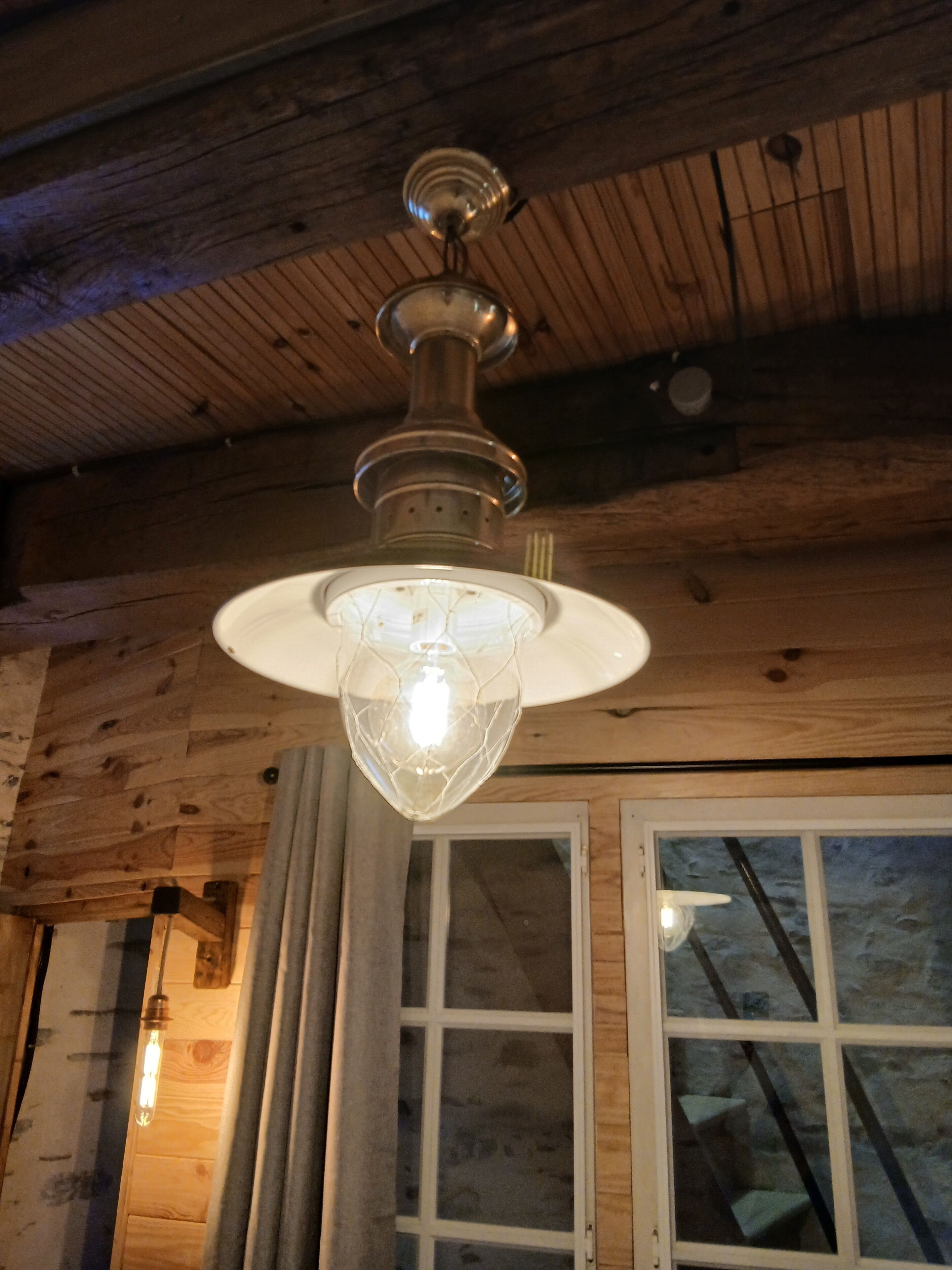 Een plafondventilator met een lamp in een houten kamer met een raam.
