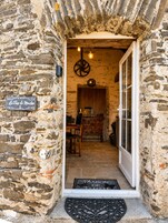 Entrada de um edifício de pedra com uma porta, um letreiro com a inscrição 'La Tour du Moulin' e um tapete com a etiqueta 'Maison de Famille'.