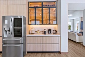 A modern kitchen with a stainless steel refrigerator, a glass-fronted cabinet with kitchenware, and a countertop with a coffee maker. - Upstay Contemporary Retreat w Pool, BBQ & Backyard (Davenport)