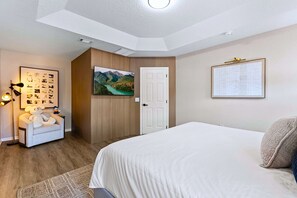 A hotel room with a bed, a desk, a chair, a lamp, and a wall with pictures. - Upstay Contemporary Retreat w Pool, BBQ & Backyard (Davenport)