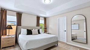 Quarto com cama, mesas de cabeceira, espelho e vista para o exterior.