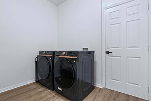 A laundry room with two front-loading washing machines and a white door. - Upstay Contemporary Retreat w Pool, BBQ & Backyard (Davenport)