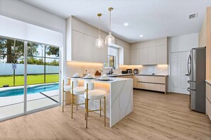 A modern kitchen with a central island, bar stools, and a view of a swimming pool. - Upstay Contemporary Retreat w Pool, BBQ & Backyard (Davenport)