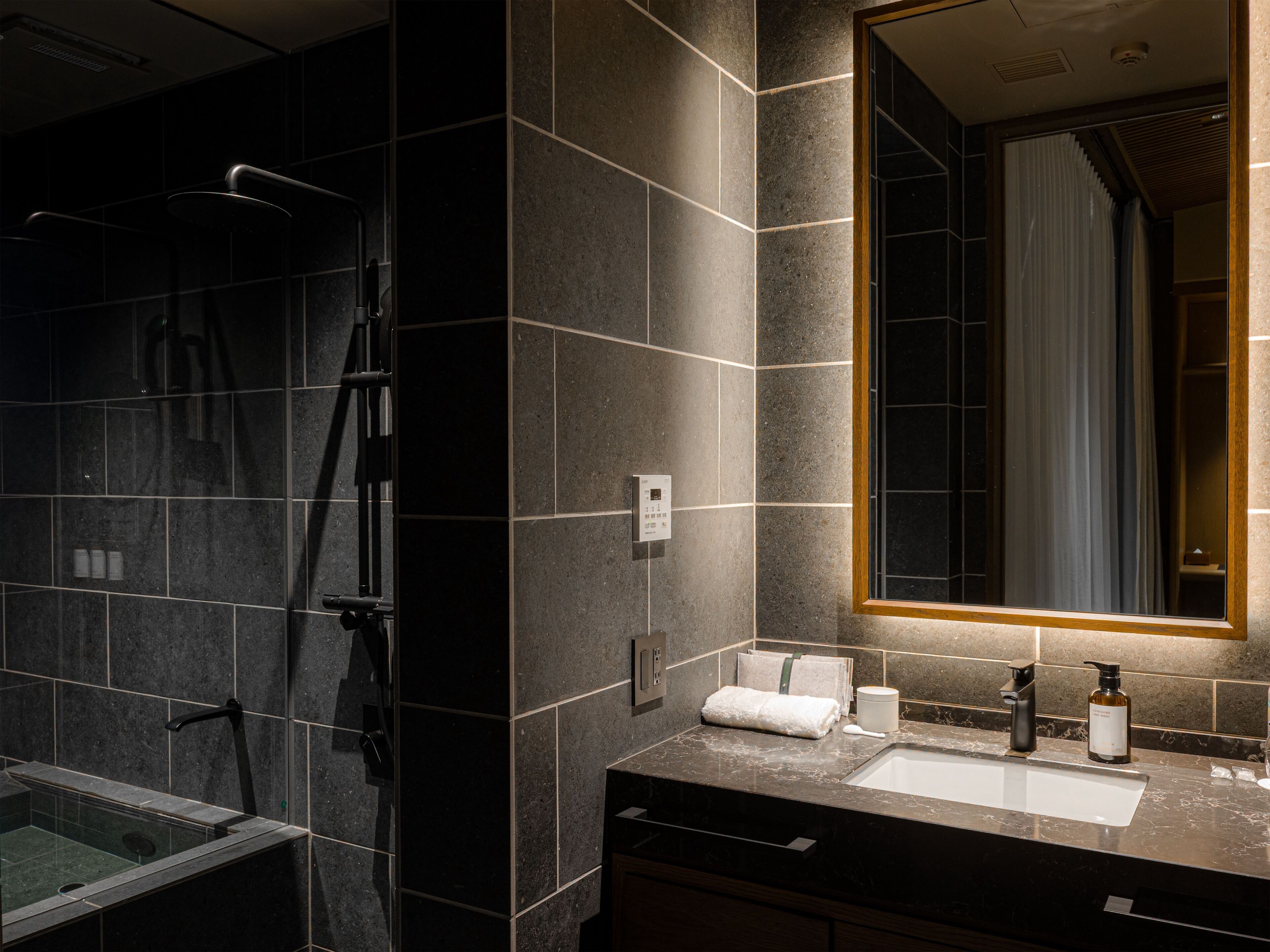 Un baño moderno con ducha envuelta en vidrio, tocador con lavamanos y espejo con luz superior.