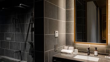 Un baño moderno con ducha envuelta en vidrio, tocador con lavamanos y espejo con luz superior.