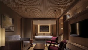 A modern hotel room with a bed, sofa, armchair, TV, and artwork.