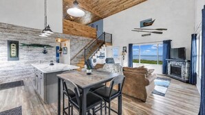 A spacious living area with a wooden ceiling, a kitchen with a white countertop, a sofa, and a fireplace. - Peaceful Cobalt Cottage on the Bay in Oconto (Oconto)
