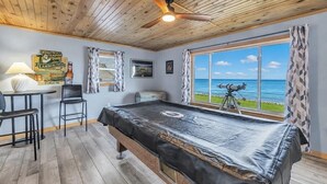 A pool table in a room with a wooden ceiling, a telescope, and a view of the ocean. - Peaceful Cobalt Cottage on the Bay in Oconto (Oconto)