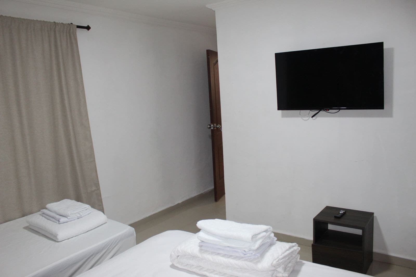 Habitación de hotel con cama, televisor montado en la pared, mesita de noche pequeña y puerta que da a un baño.