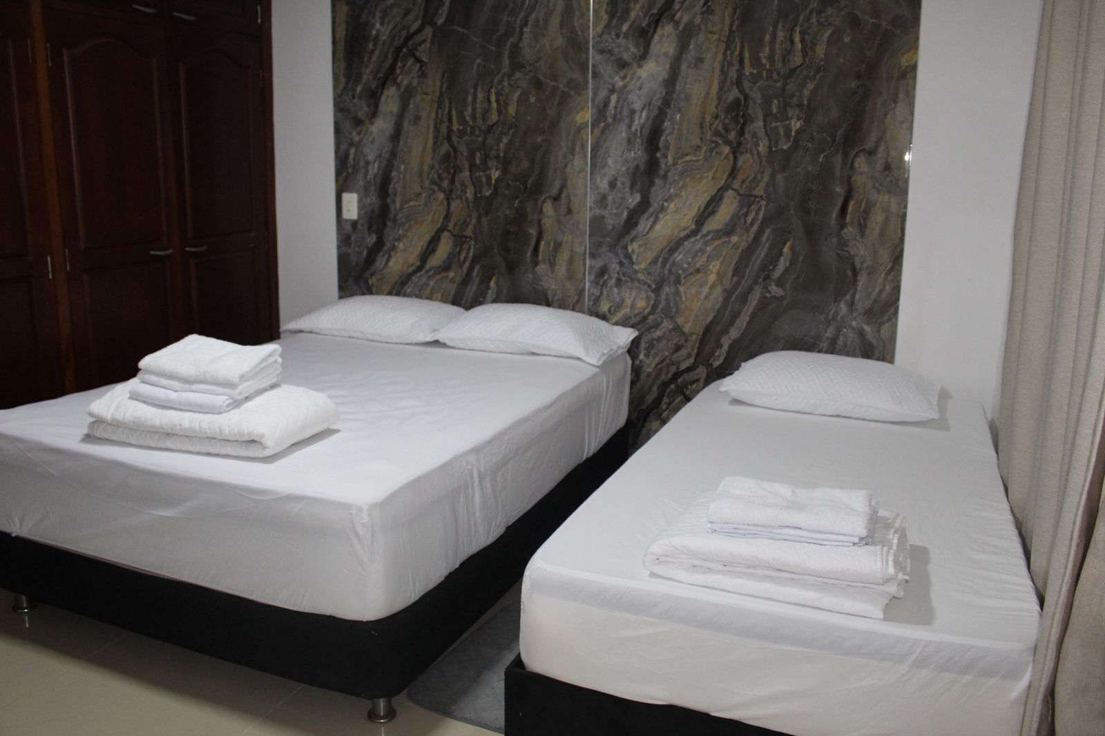 Ein Hotelzimmer mit zwei Betten, jeweils mit weißen Laken und Handtüchern, einer Wand im Marmoroptik und einem Holzschrank.