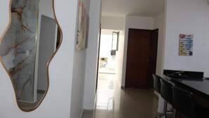 A hallway with a marble wall, a wooden-framed mirror, and a door leading to a kitchen area.