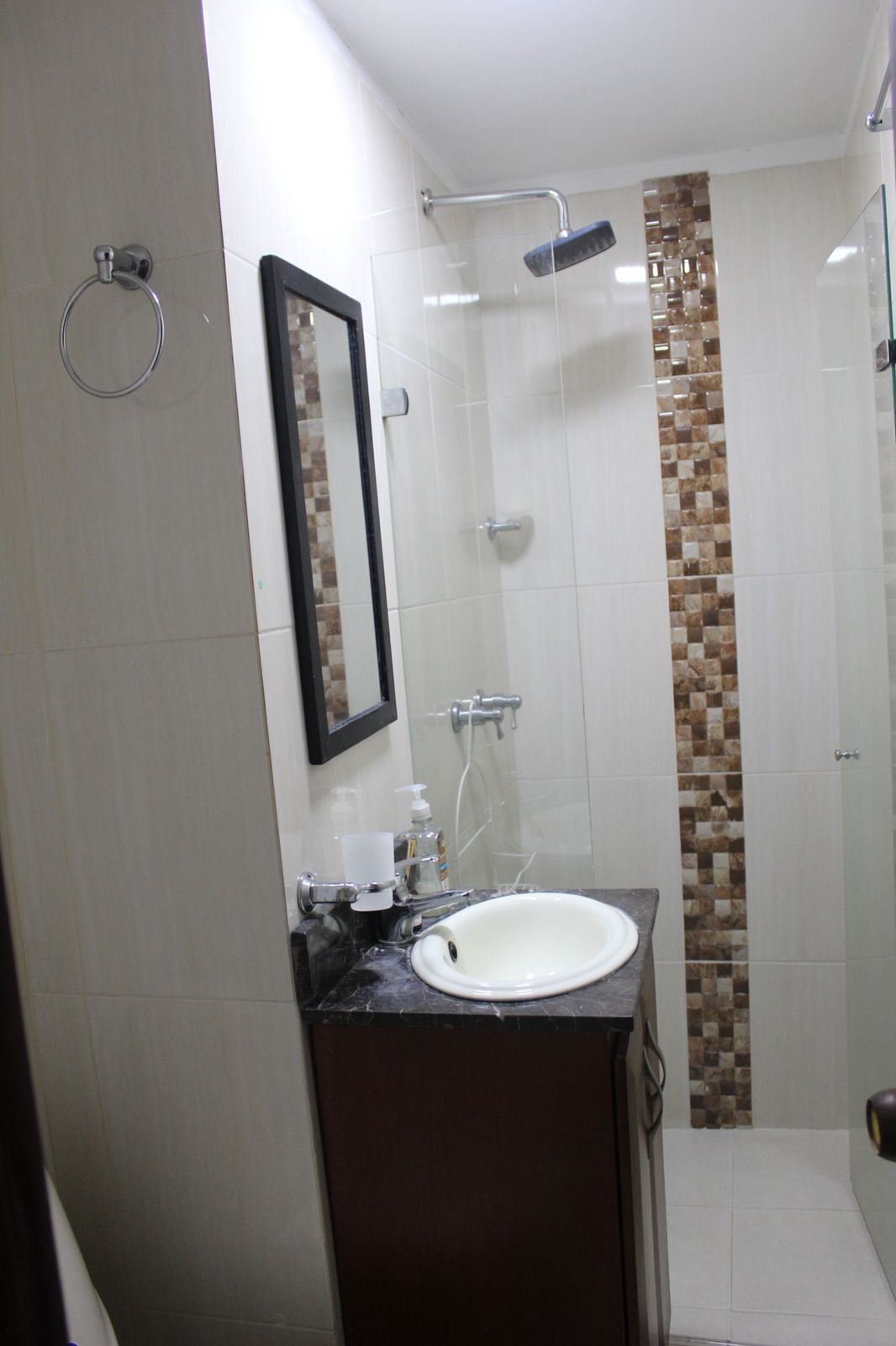 A bathroom with a white sink, a glass shower enclosure, and a tiled shower wall.