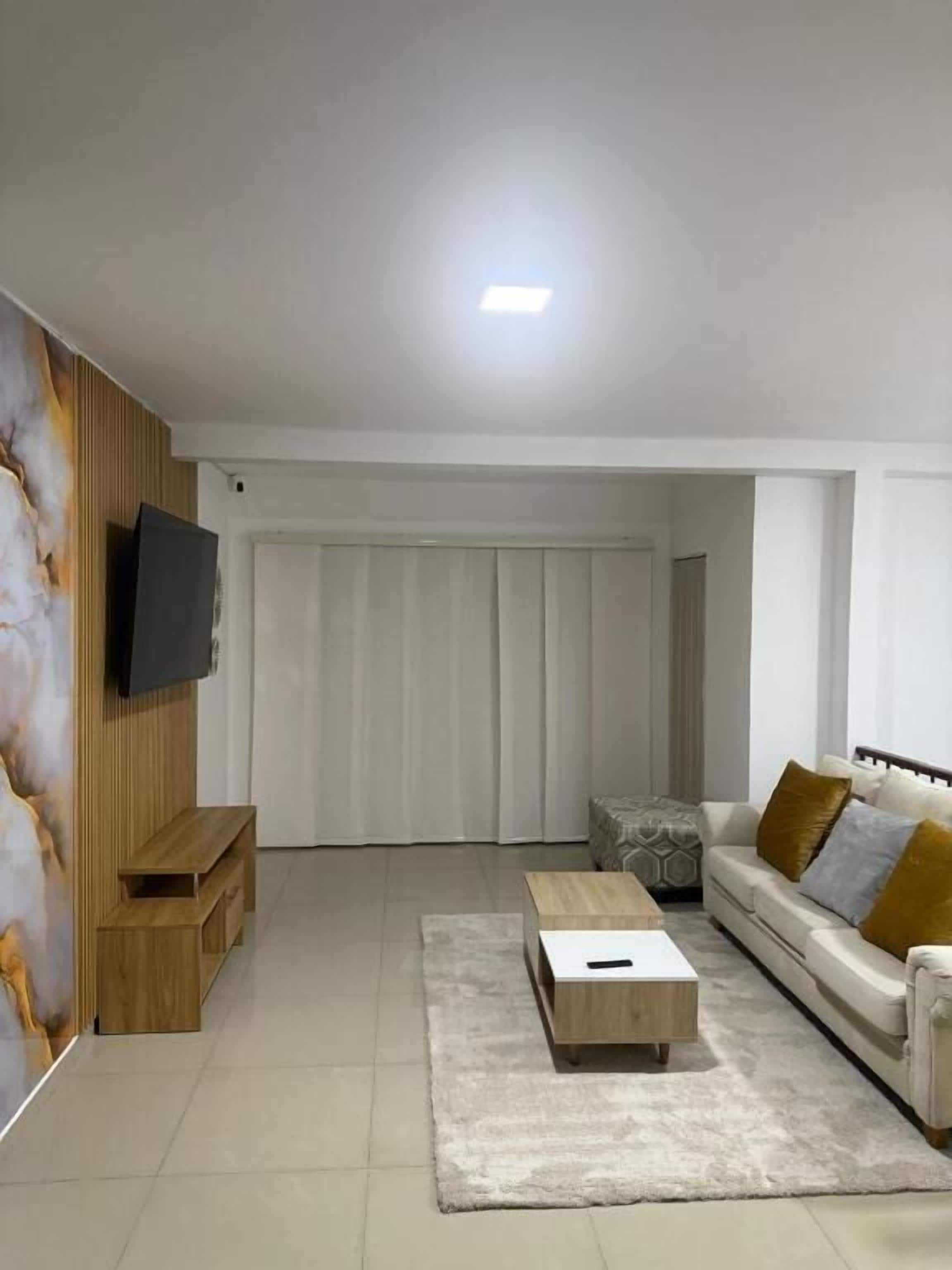 Una sala de estar moderna con una televisión de pantalla plana, un sofá con cojines, una mesa de centro y un mueble de televisión de madera.