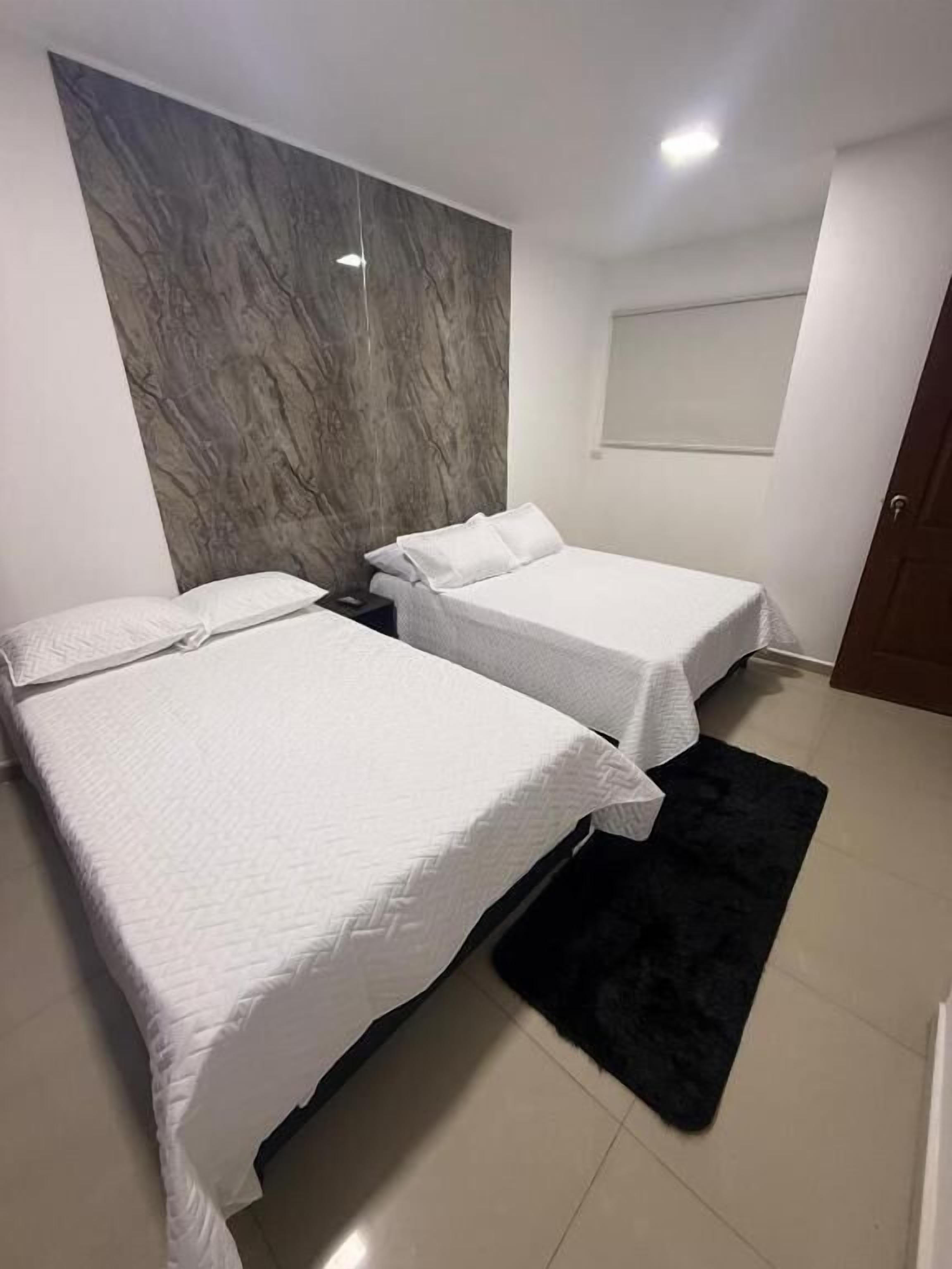 A bedroom with two beds, a dark rug, and a marble wall.