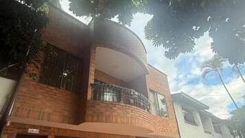 A two-story house with a curved balcony, a brick facade, and a tiled driveway.