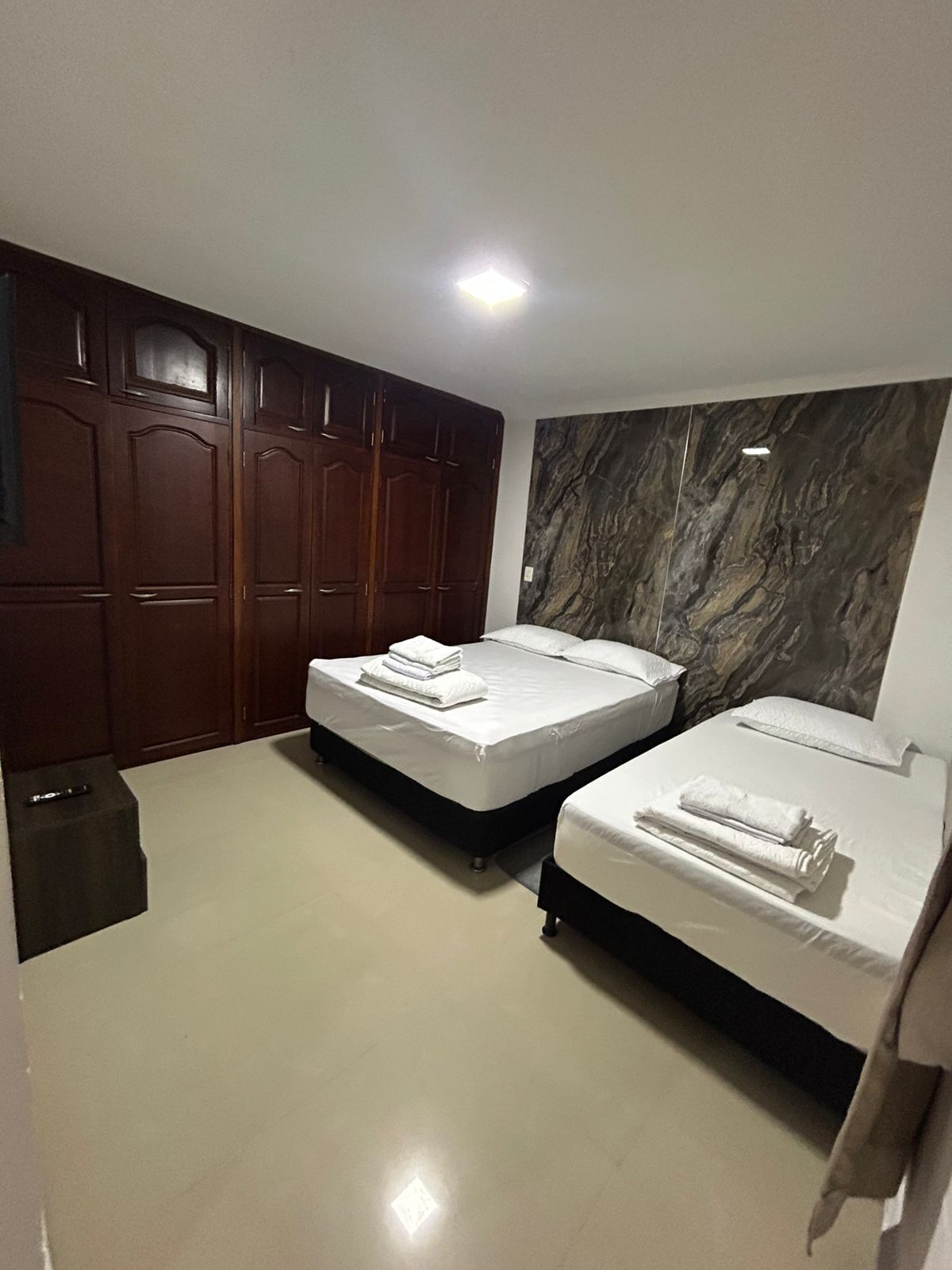 A room with two beds, a wardrobe, and a marble wall.