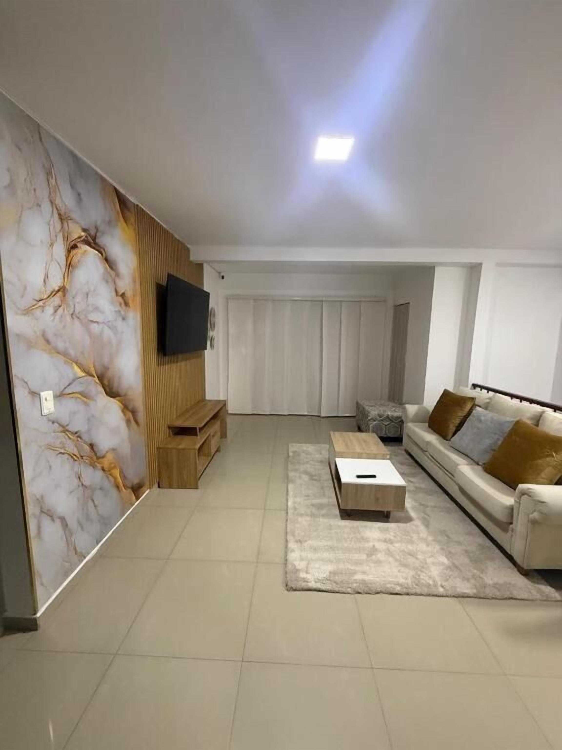 A modern living room with a sofa, a coffee table, a TV, and a patterned wall.