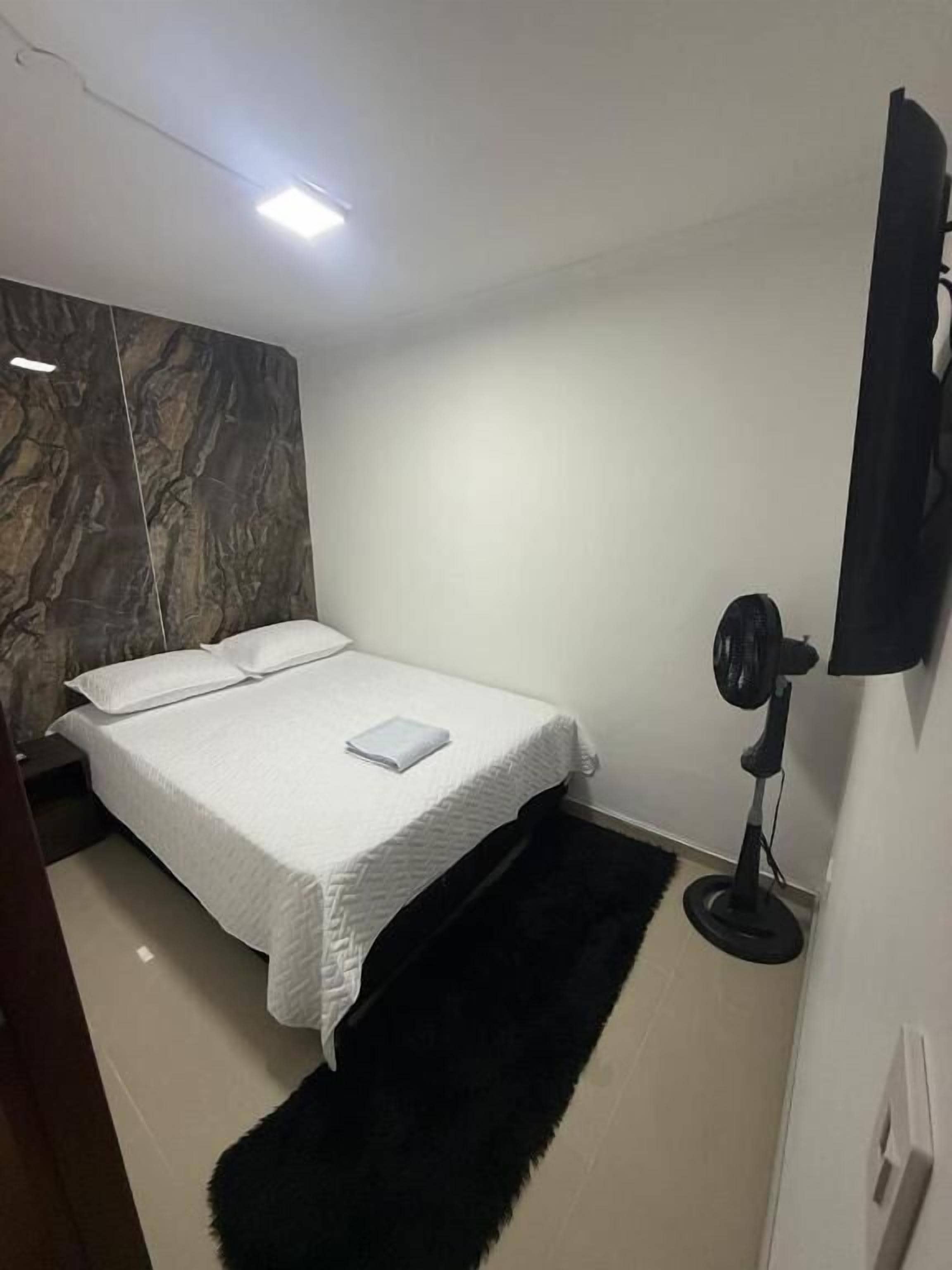 A bedroom with a bed, a black rug, a wall-mounted TV, and a ceiling light.