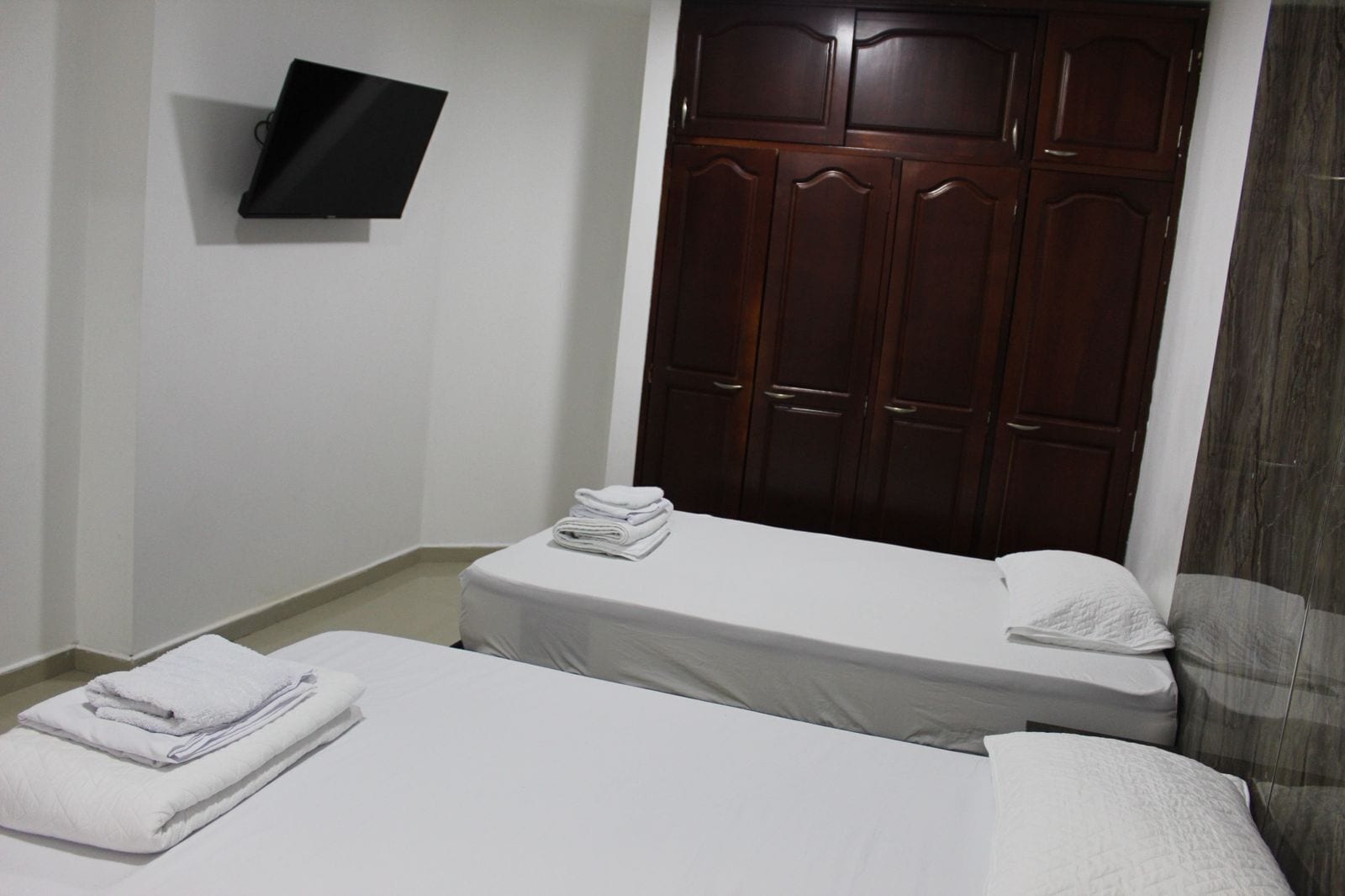 A hotel room with two beds, a wardrobe, and a flat-screen TV mounted on the wall.