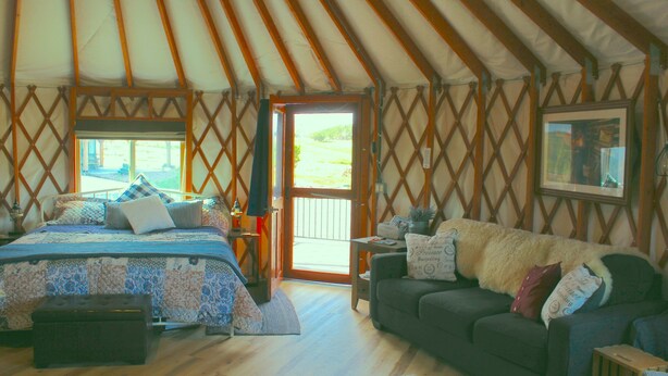 L’intérieur d’une yourte, avec un lit, un canapé et une porte donnant sur l’extérieur.