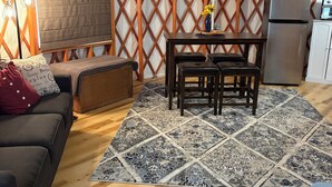 Un espace de vie chaleureux comprenant un canapé, une table à manger avec des chaises, un coin cuisine avec un réfrigérateur et un tapis à motifs.