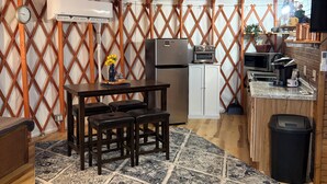 L’intérieur chaleureux d’une yourte, avec une table en bois, des chaises, un réfrigérateur, un poêle et un plan de travail de cuisine.