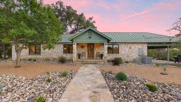 A stone house with a green roof, a stone pathway, and a tree in the foreground.