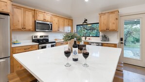 A kitchen with wooden cabinets, a large island, a refrigerator, a microwave, and a coffee maker. - Twisted Cedar Retreat - River views w/Firepit! (Ingram)