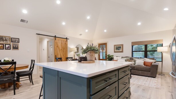 A spacious kitchen with a large island, a dining area with a wooden table and chairs, a living area with a sofa and a TV, and a sliding barn door. - Twisted Cedar Retreat - River views w/Firepit! (Ingram)