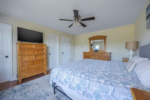 Ein Schlafzimmer mit Bett, Kommode, Fernseher, Deckenventilator und Spiegel.