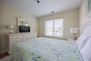 A bedroom with a bed, a dresser, a television, a window with blinds, and a lamp. - 5600 - On the Sunny Side Soundside 3BR retreat with deck, Wi-Fi, and golf views. (Nags Head)