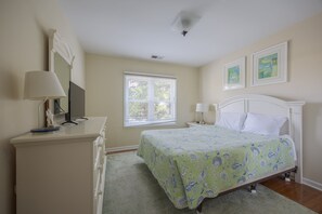 Een slaapkamer met een bed, een dressoir, een televisie en een raam met jaloezieën.