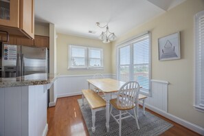 Een keuken met een inbouwkoelkast, een eettafel met stoelen en een raam met jaloezieën.