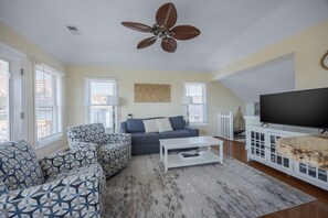 A living room with a ceiling fan, a sofa, a coffee table, and a TV. - 5600 - On the Sunny Side Soundside 3BR retreat with deck, Wi-Fi, and golf views. (Nags Head)