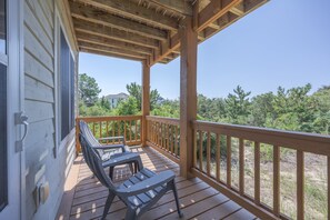 A wooden deck with two chairs and a table, overlooking a landscape with trees and houses. - 5600 - On the Sunny Side Soundside 3BR retreat with deck, Wi-Fi, and golf views. (Nags Head)
