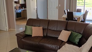 Een woonkamer met een bruine leren bank, een glazen salontafel en uitzicht op de eetruimte.