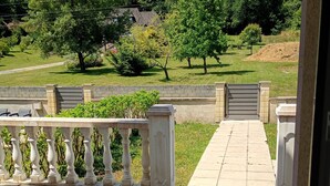 Een betegeld balkon met uitzicht op een aangelegde tuin en een poort.