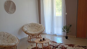 Een kamer met twee rieten stoelen, een klein houten tafeltje, een kleden van runderleer, een potplant en een deur.