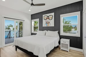 Ein Schlafzimmer mit einem Bett, einem Nachttisch, einem Deckenventilator, einem großen Fenster und Blick auf einen Balkon mit Pool.